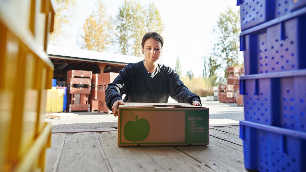 A farmer loads a box of apples onto a truck.