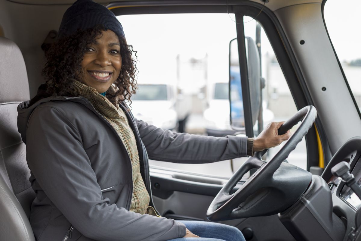 A female driver smiles behind the wheel.