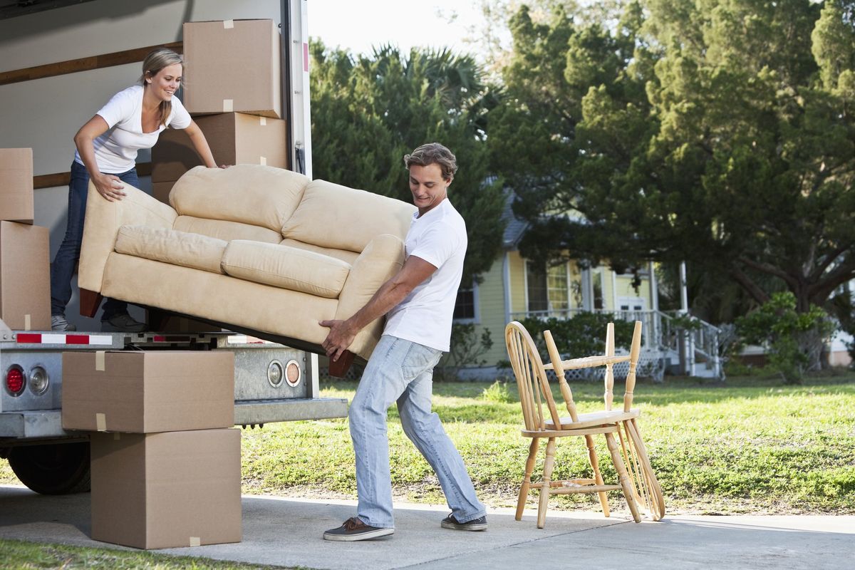 A man and a woman load a love seat into the back of a box truck.