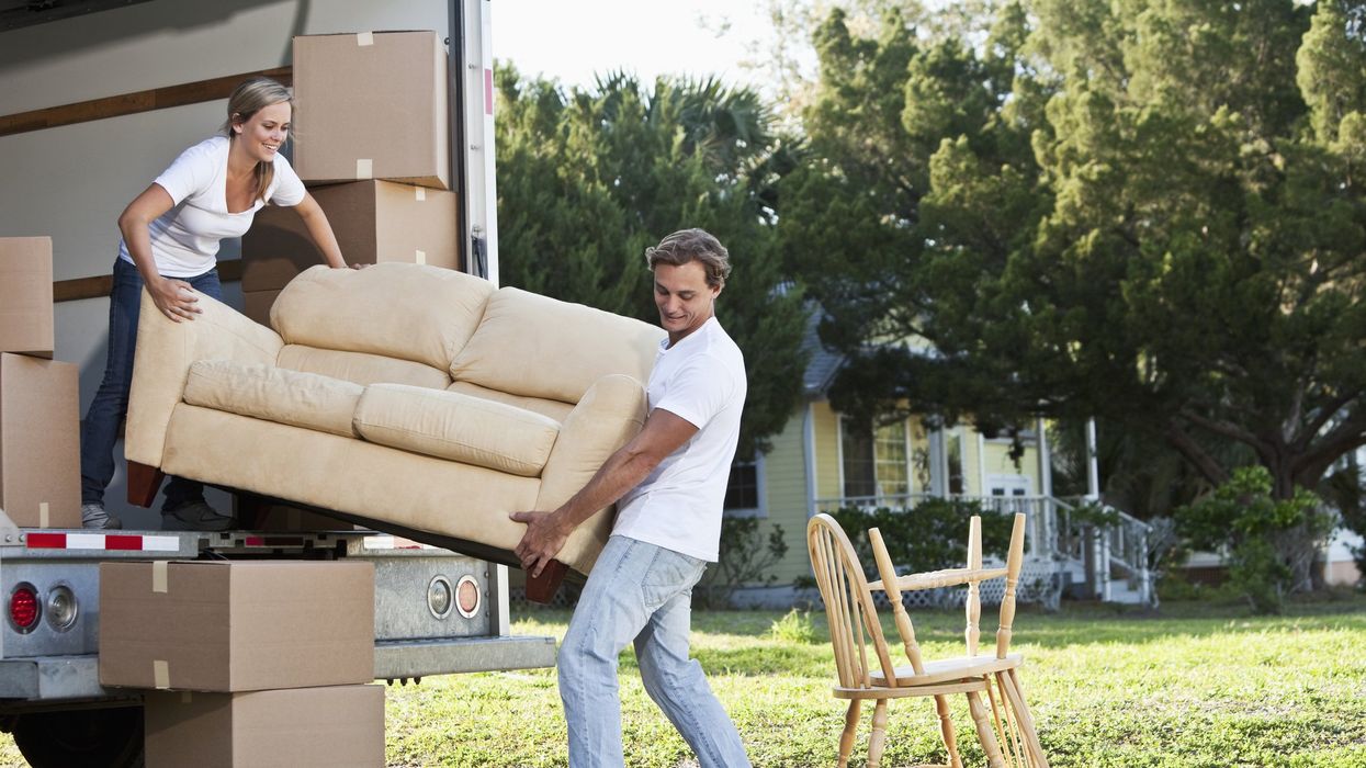 A man and a woman load a love seat into the back of a box truck.