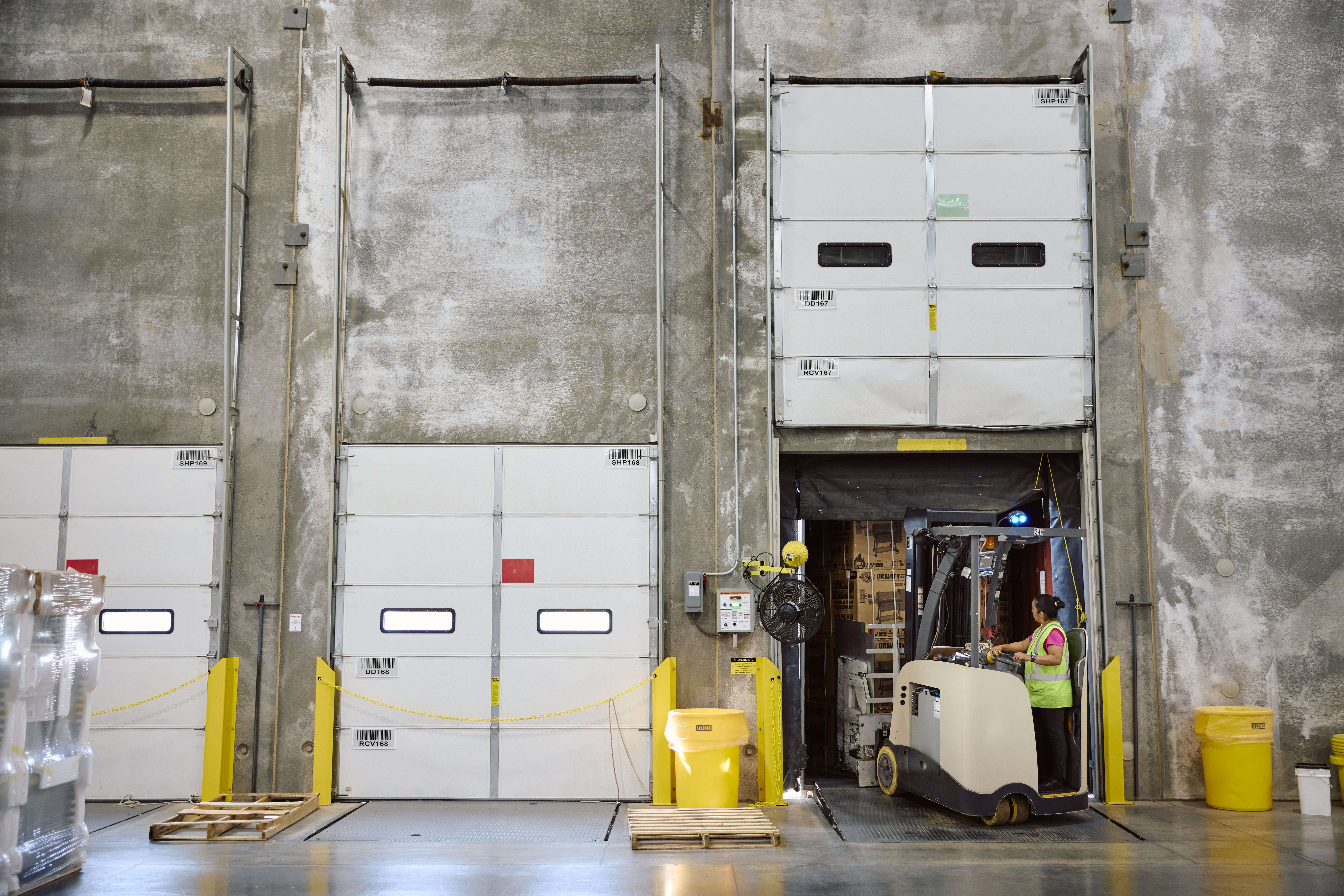 A retail warehouse worker uses a forklift to move boxes in a warehouse.