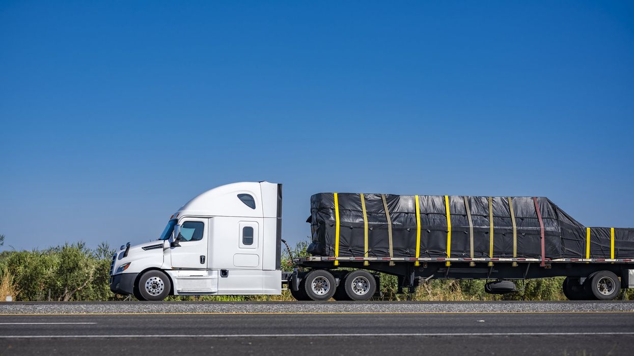 A semi truck on the road with cargo secured to the trailer.