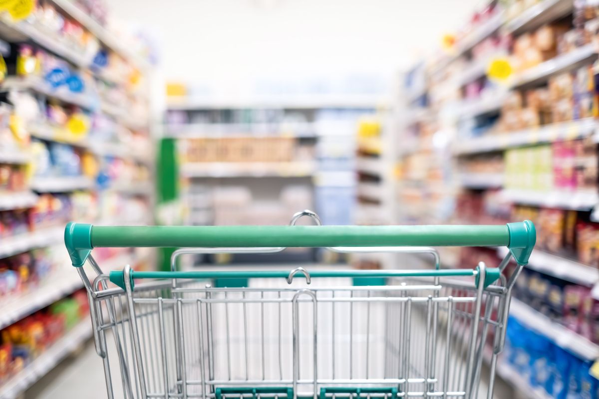 A shopping cart with a green handle sitting in a grocer store aisle.