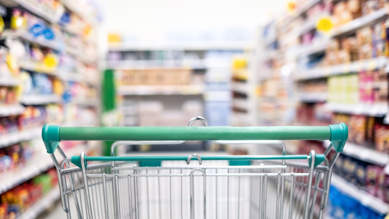 A shopping cart with a green handle sitting in a grocer store aisle.