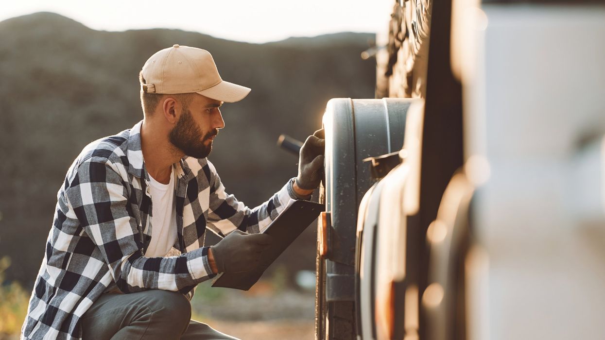 A truck driver inspects the front tires of his truck.