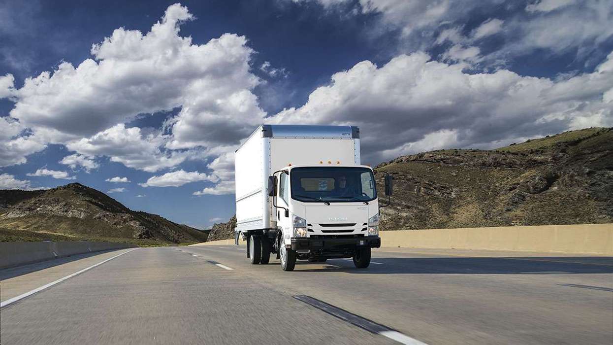 A white cabover truck drives up a road under a blue cloudy sky.