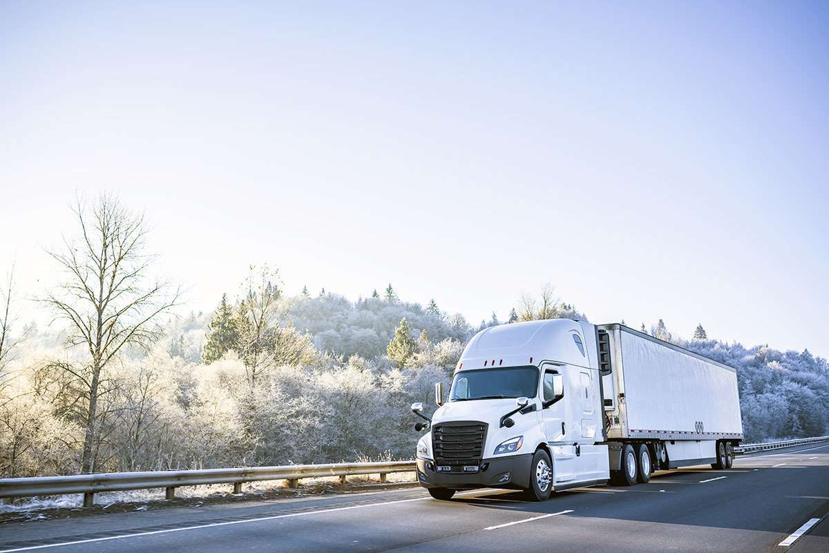 A white semi-truck drives on a freeway amid frost-covered trees.