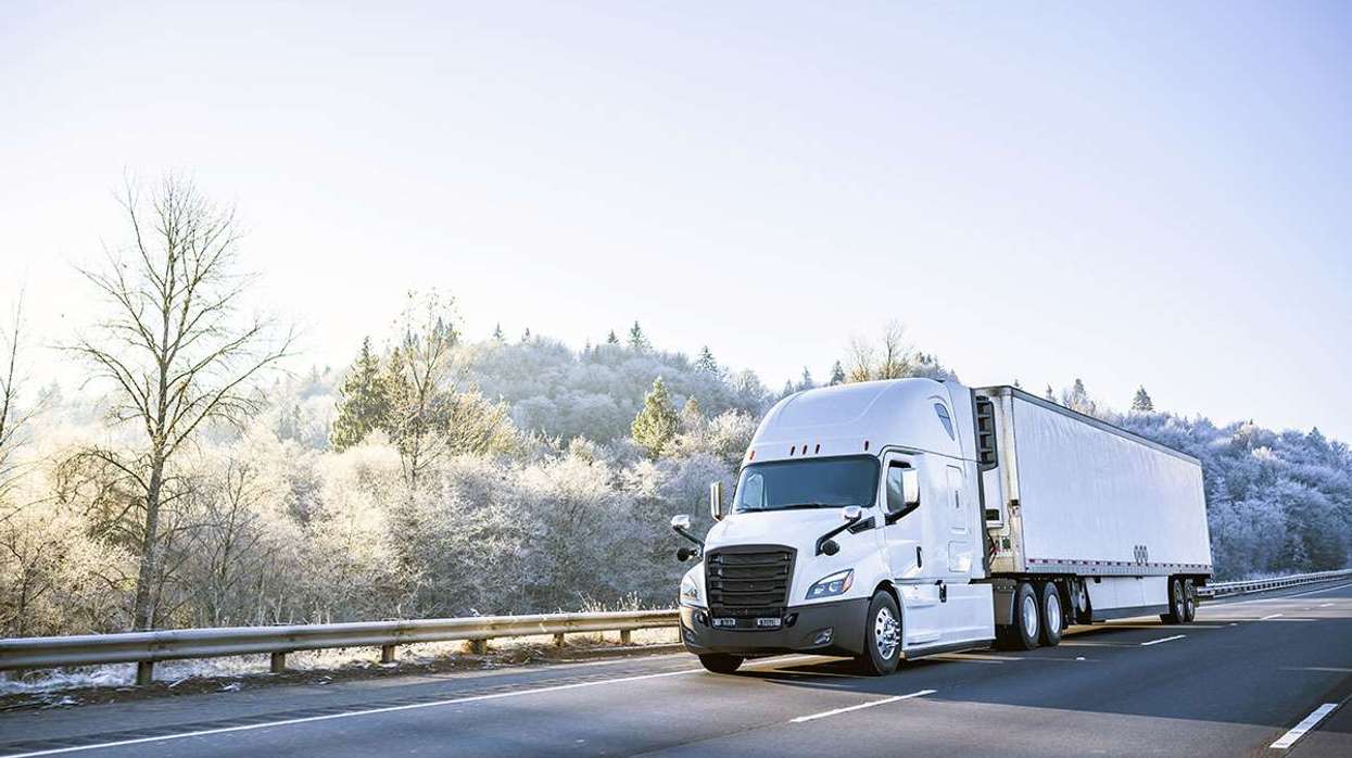 A white semi-truck drives on a freeway amid frost-covered trees.