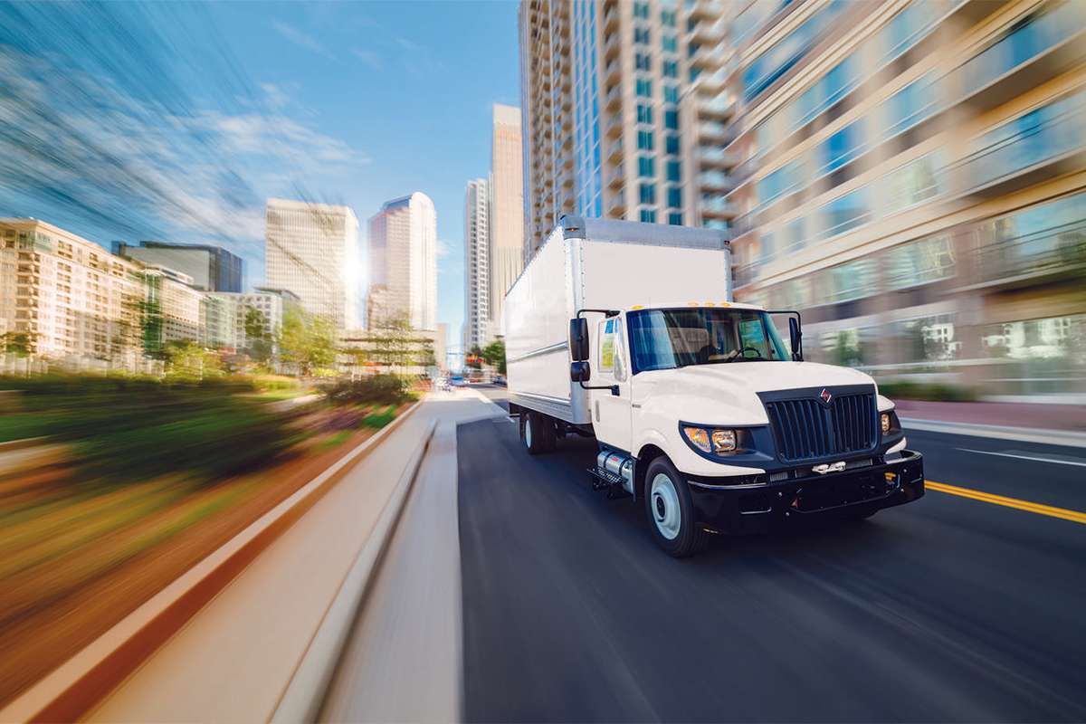 A white used box truck drives down a city street.