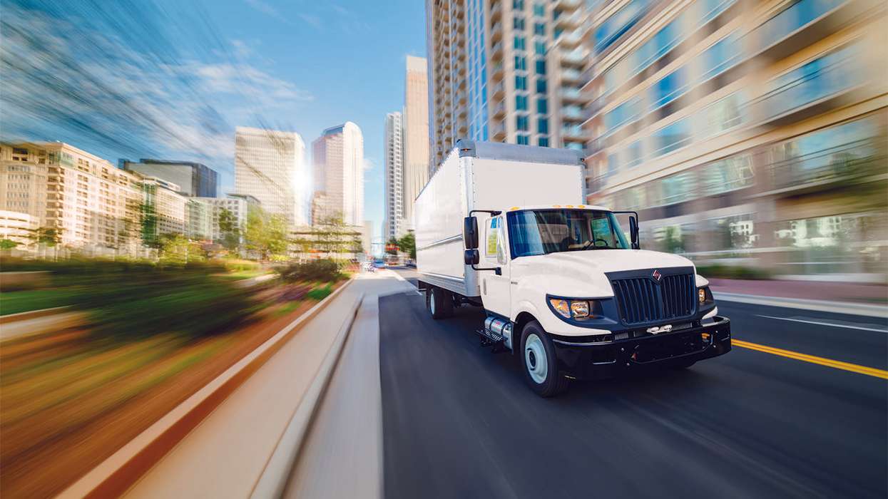 A white used box truck drives down a city street.