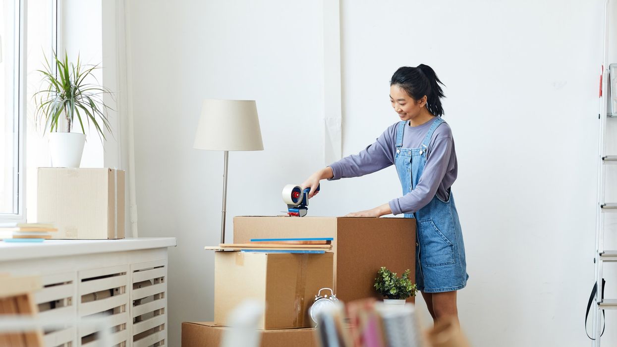 A woman tapes a cardboard box shut after packing it.