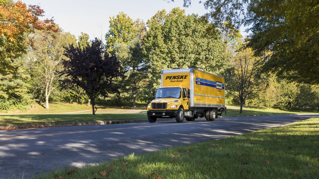 A yellow 26 foot Penske truck drives up a road.