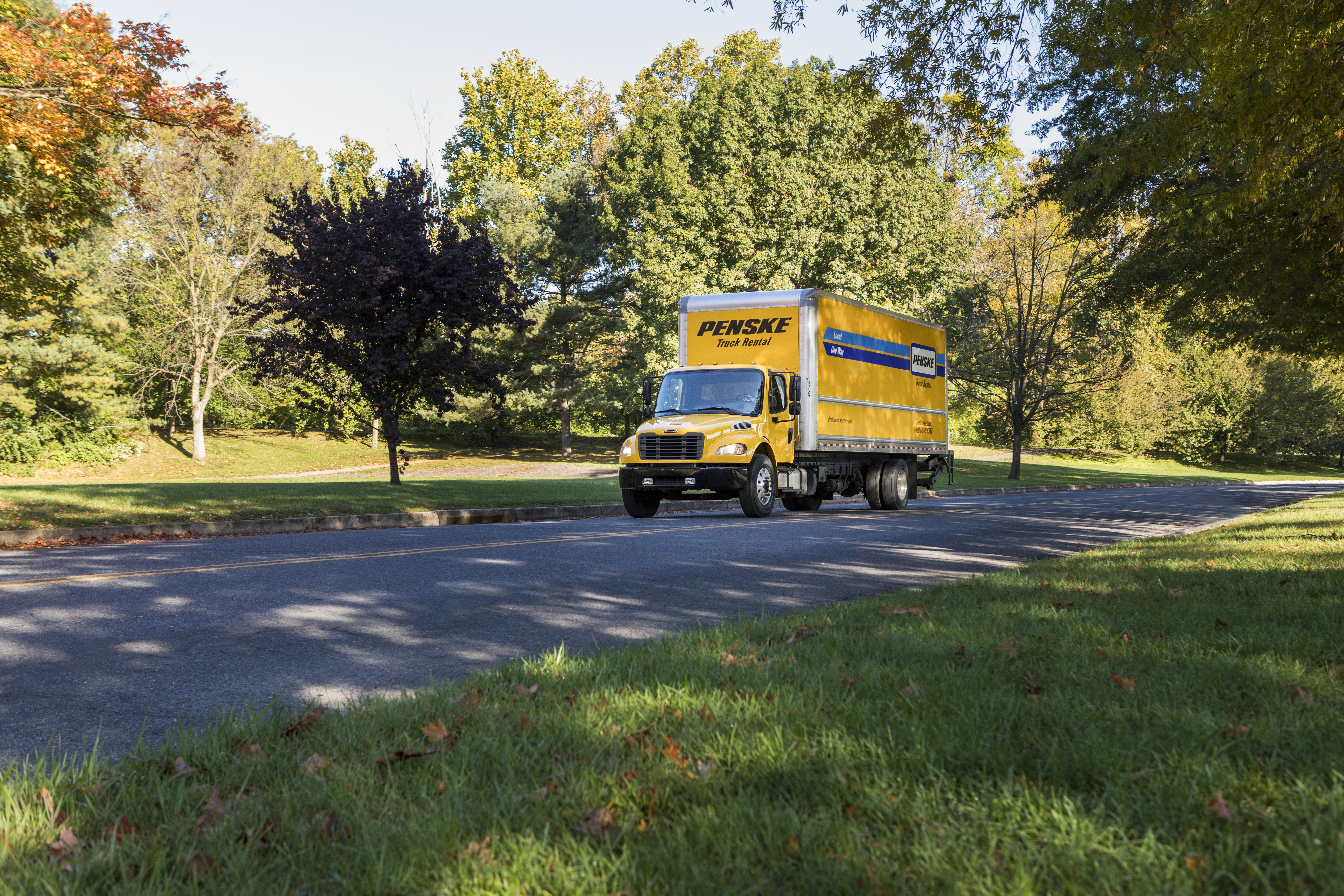 A yellow 26 foot Penske truck drives up a road.