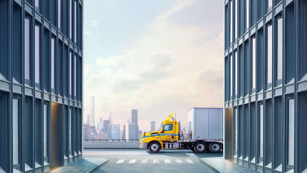 A yellow and white Penske semi-truck drives along a city road.