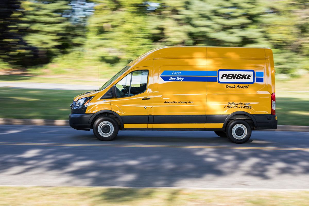 A yellow Penske cargo van drives down the road.