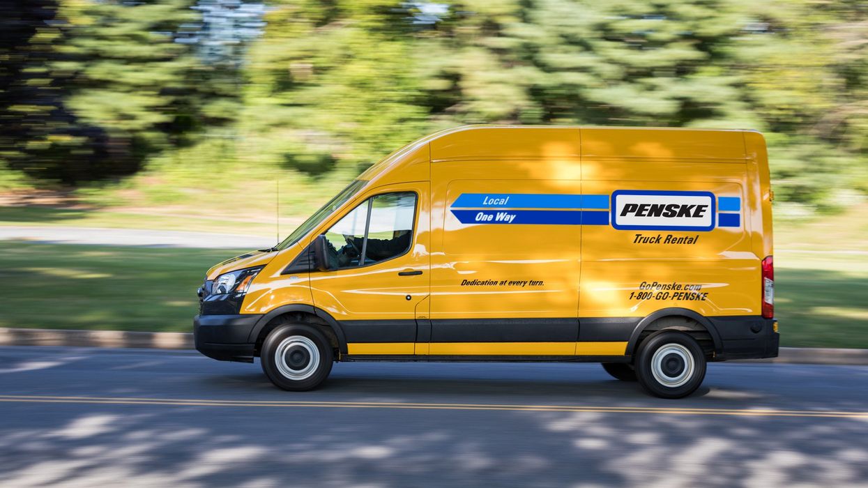 A yellow Penske cargo van drives down the road.