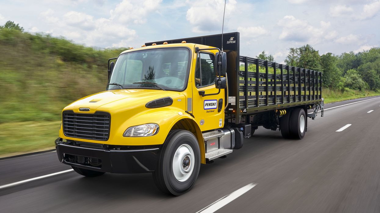 A yellow Penske flatbed truck drives on the highway.