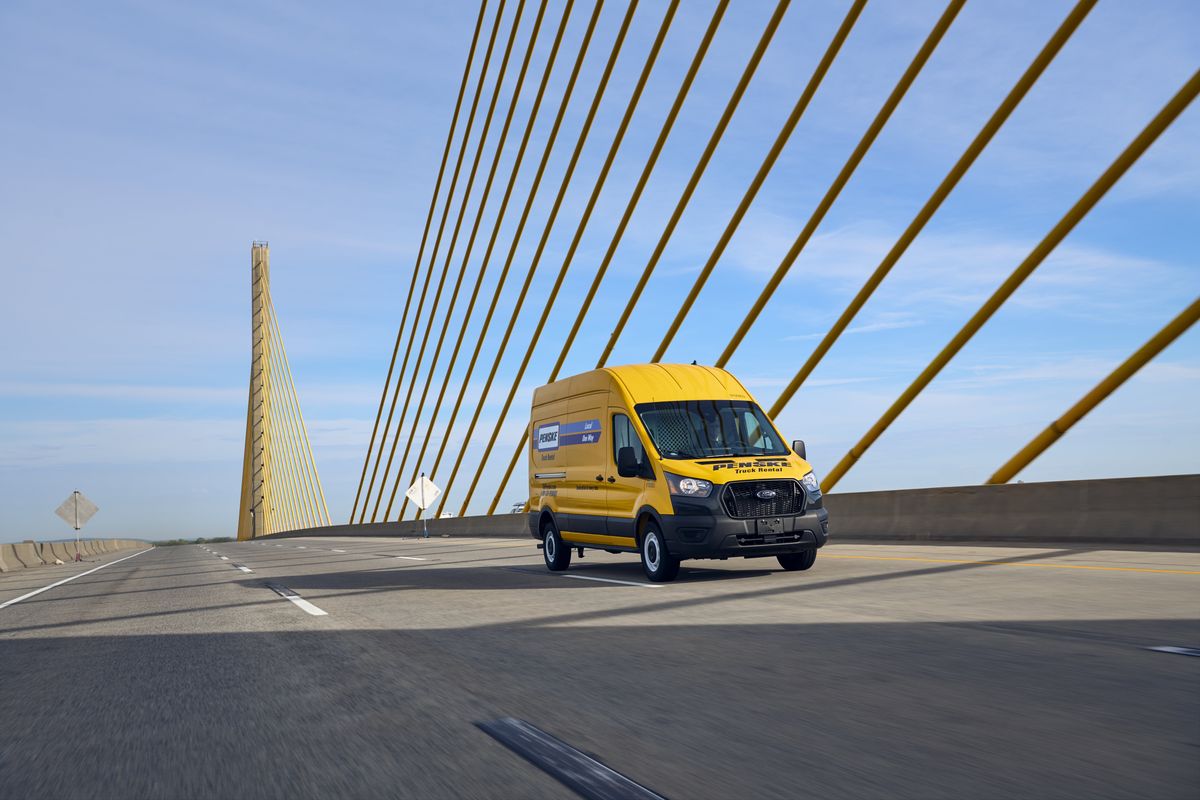 A yellow Penske van drives across a bridge