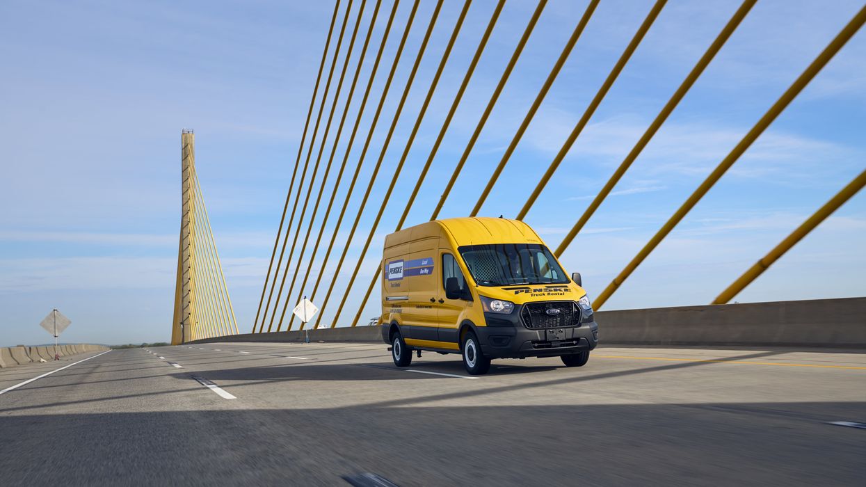 A yellow Penske van drives across a bridge