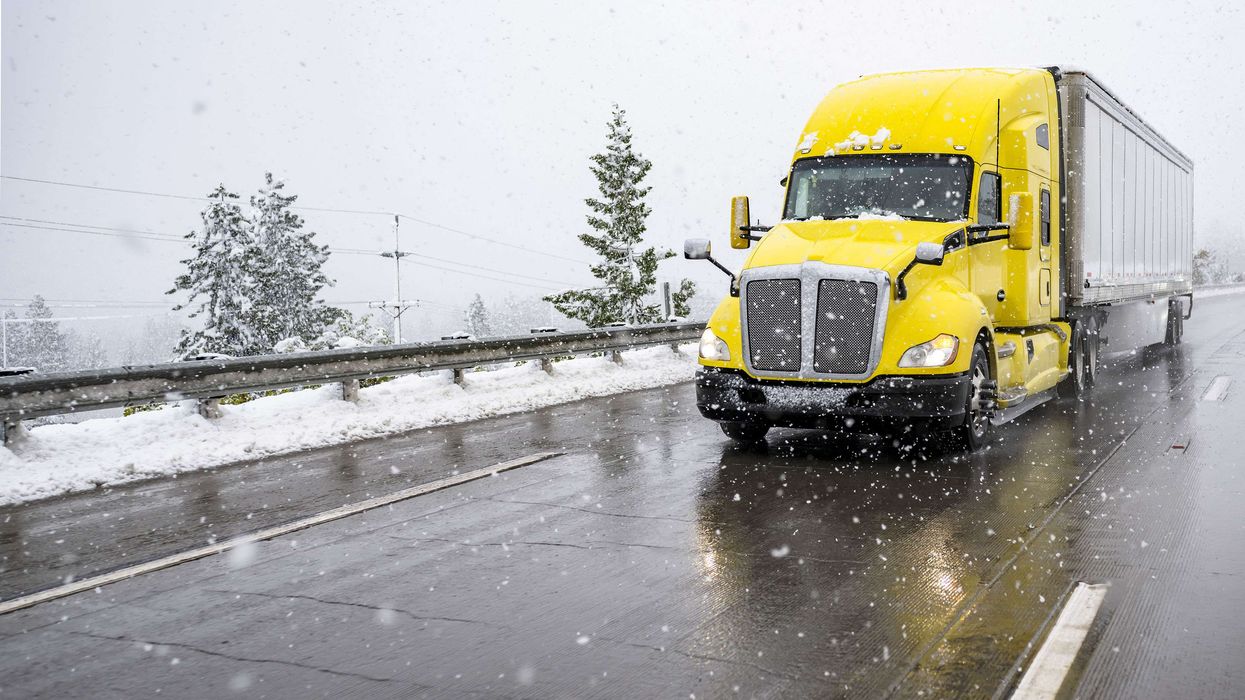 A yellow semi truck drives on a snowy road