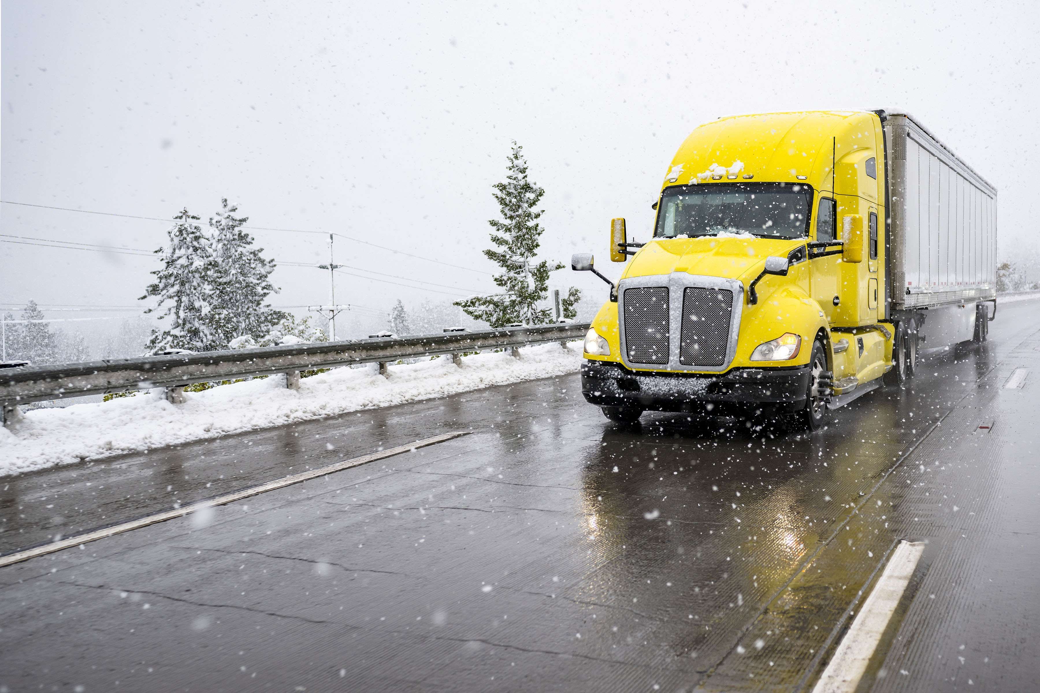 A yellow semi truck drives on a snowy road