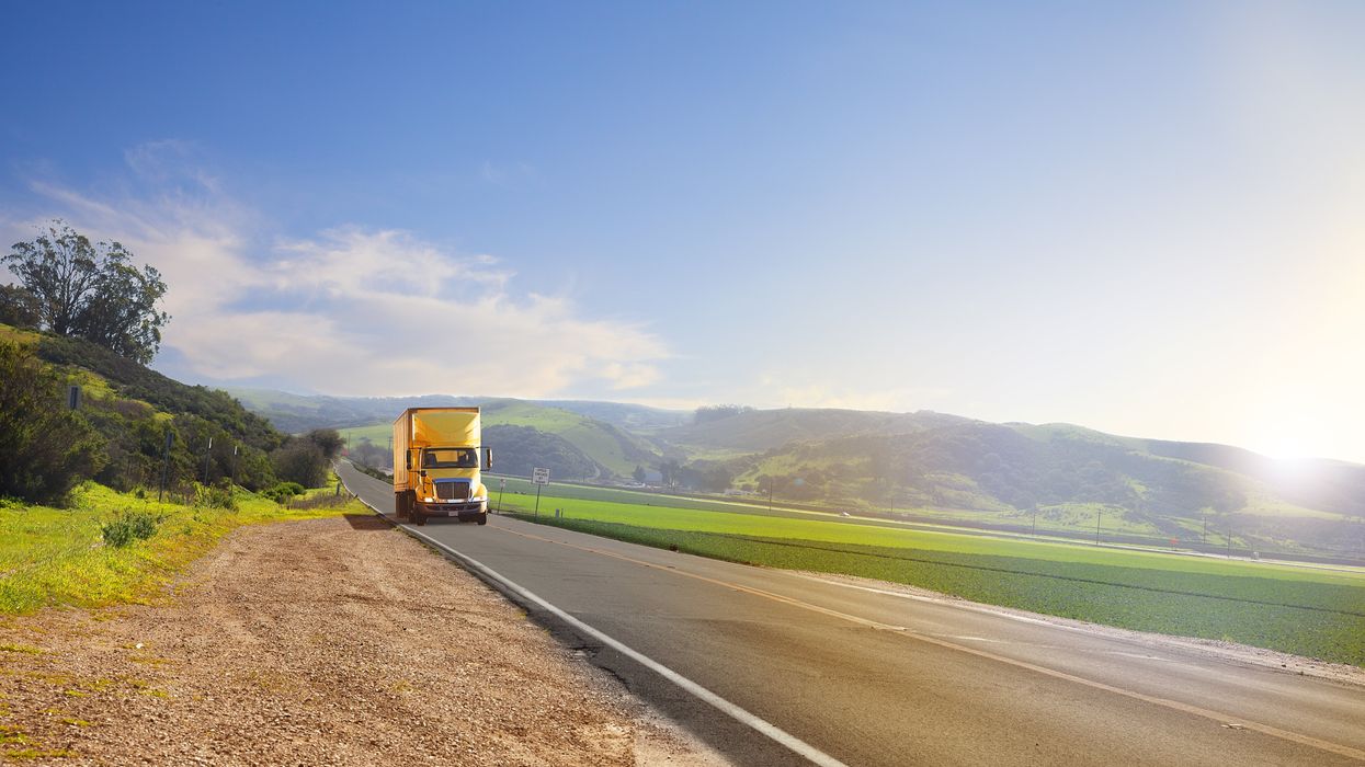 A yellow truck drives through the country on a sunny day.