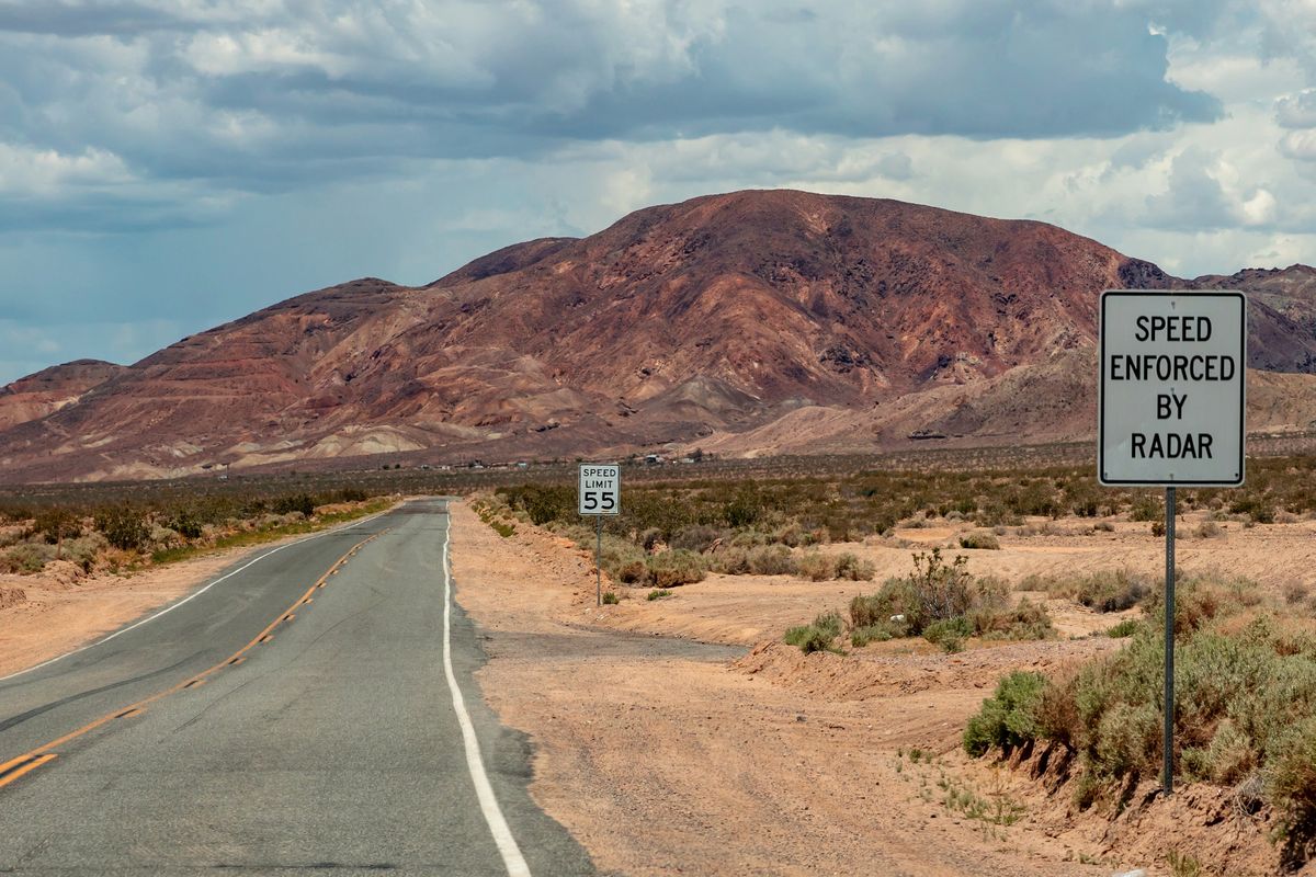 An empty desert road with a Speed Enforced By Radar sign.