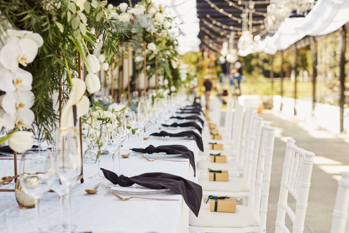 An event tablescape with black napkins and white flowers, chairs and tablecloth