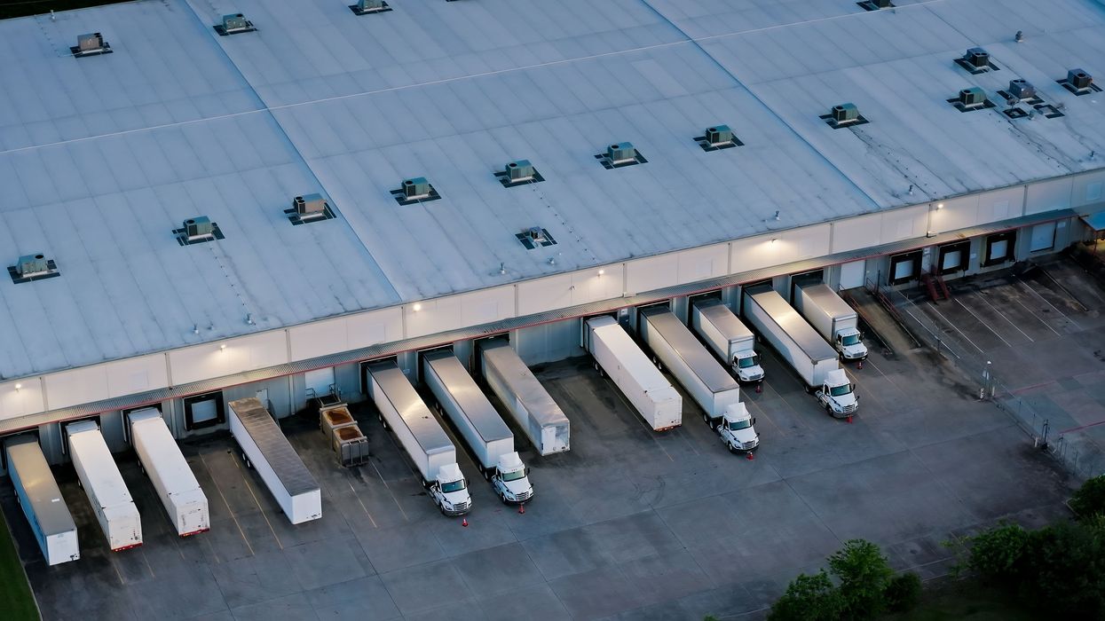 An overview shot of semi trucks and trailers parked at a warehouse.