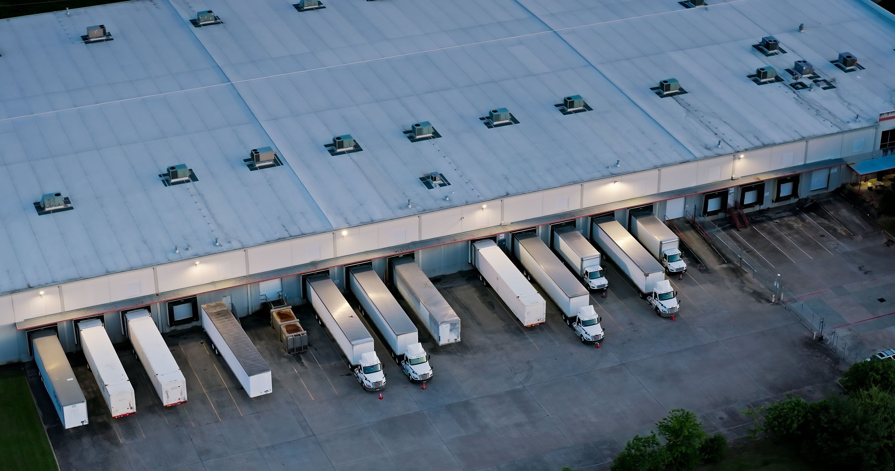 An overview shot of semi trucks and trailers parked at a warehouse.