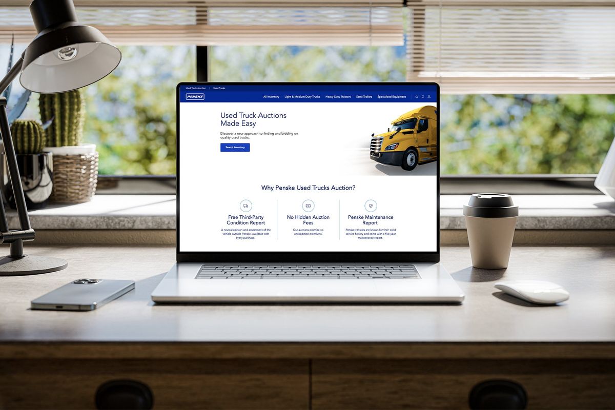 Laptop displaying Penske Used Trucks auction website on a desk.