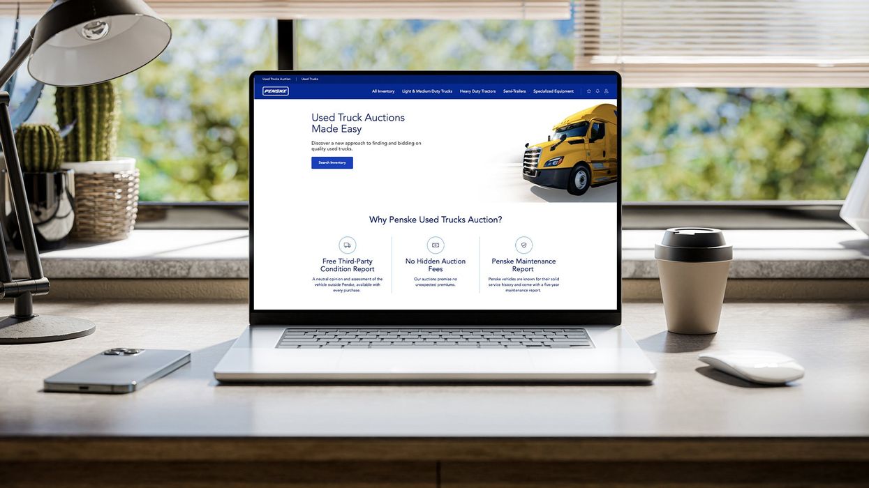 Laptop displaying Penske Used Trucks auction website on a desk.