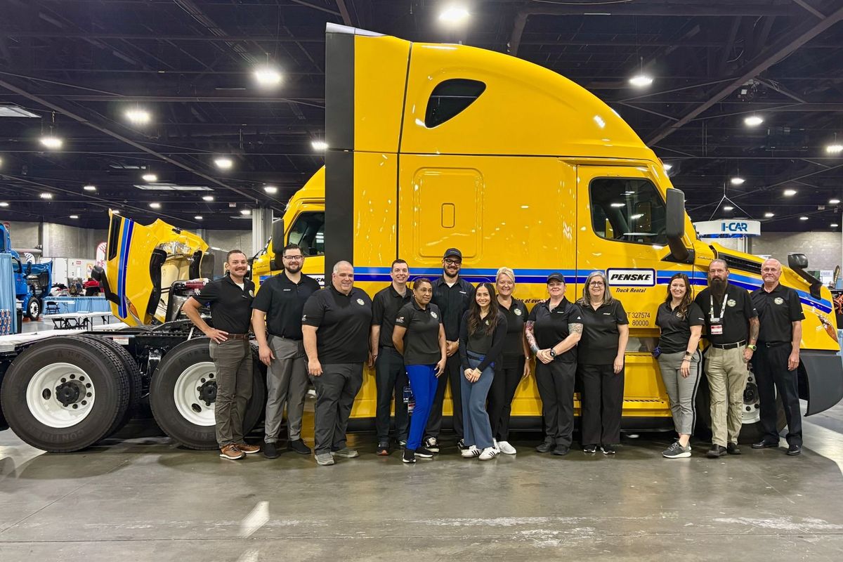 Penske employees lined up in front of a yellow Penske truck
