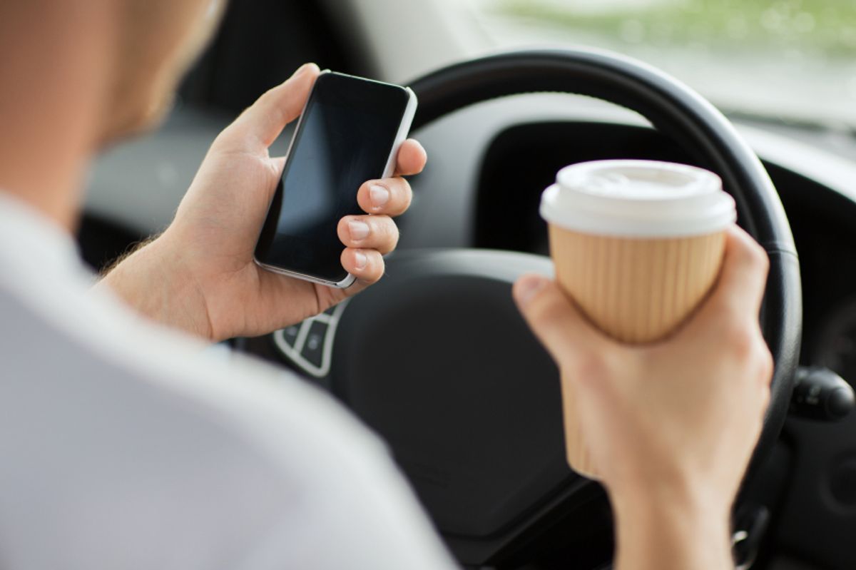 Person holding a phone and coffee while in the driver's seat.