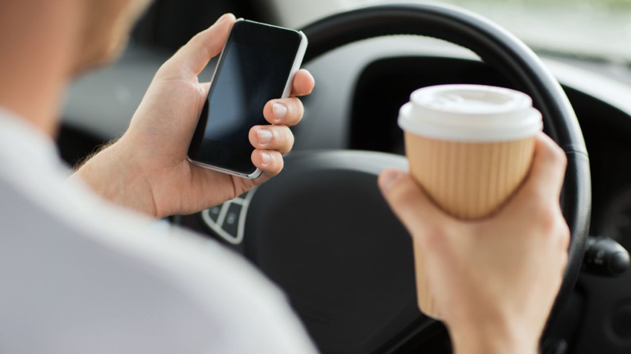 Person holding a phone and coffee while in the driver's seat.