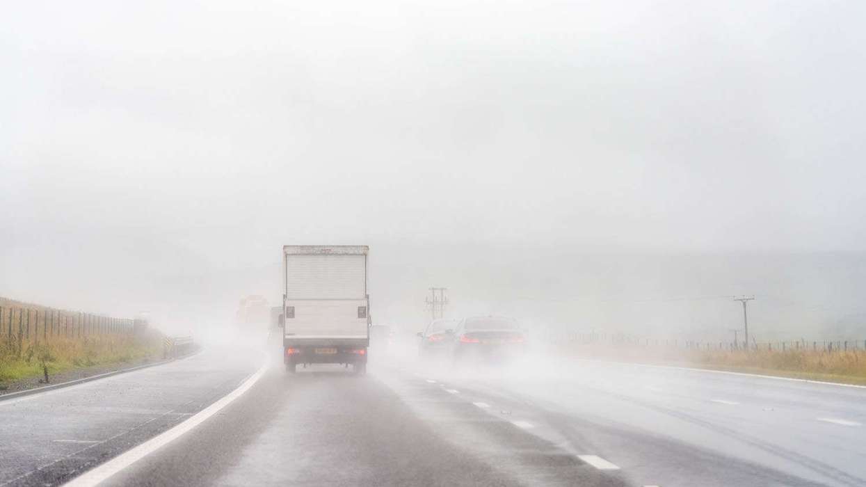 The back of a white box truck and other cars driving up a rainy, foggy road.