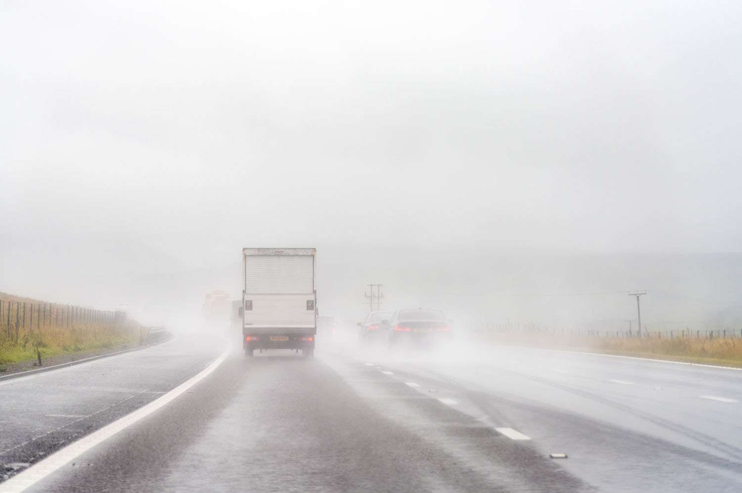 The back of a white box truck and other cars driving up a rainy, foggy road.