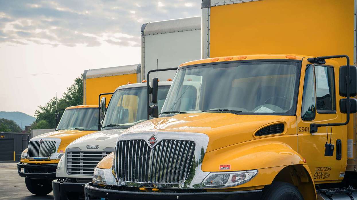 Three yellow and white used Penske box trucks are lined up in a lot.