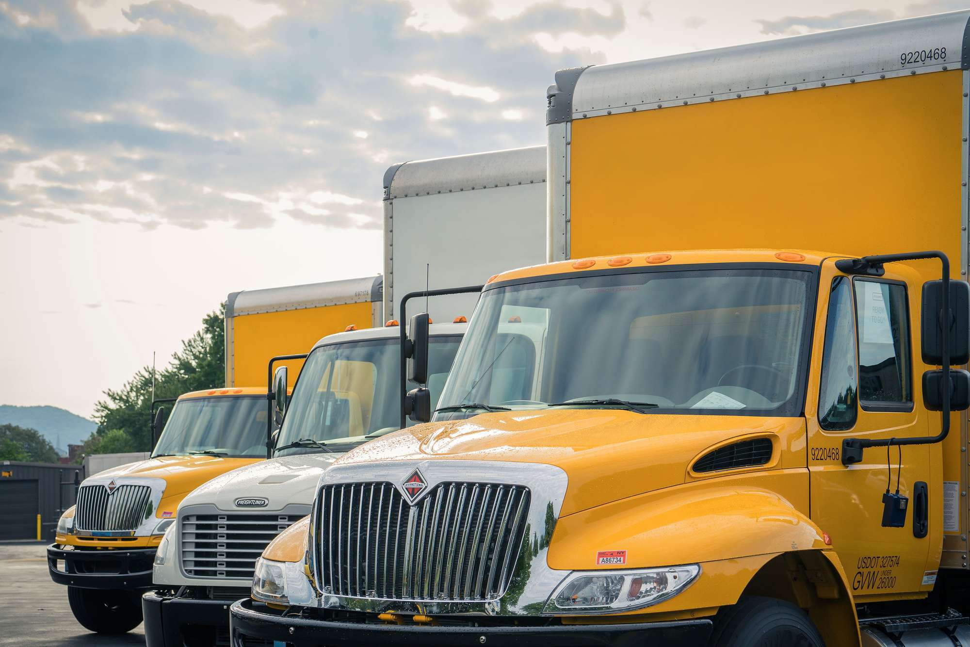 Three yellow and white used Penske box trucks are lined up in a lot.