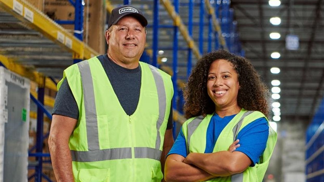 Two Penske warehouse associates stand in a distribution center aisle, showcasing teamwork and professionalism during Warehouse Associate Appreciation Week.