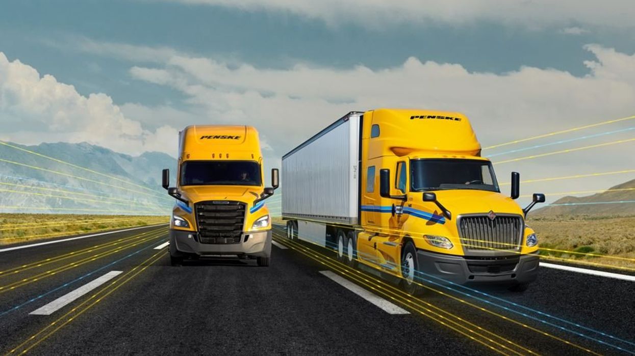 Two yellow Penske trucks driving down the highway