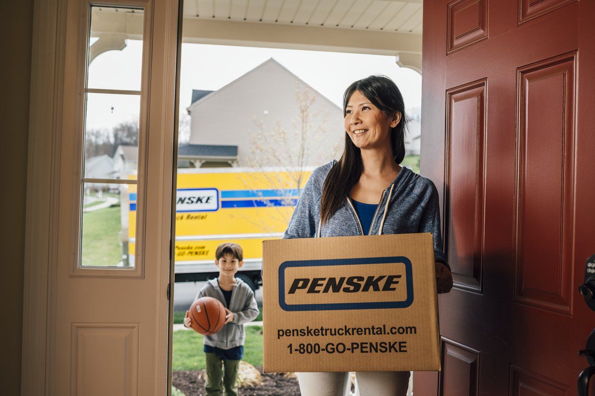 Woman walking through front door carrying a moving box.