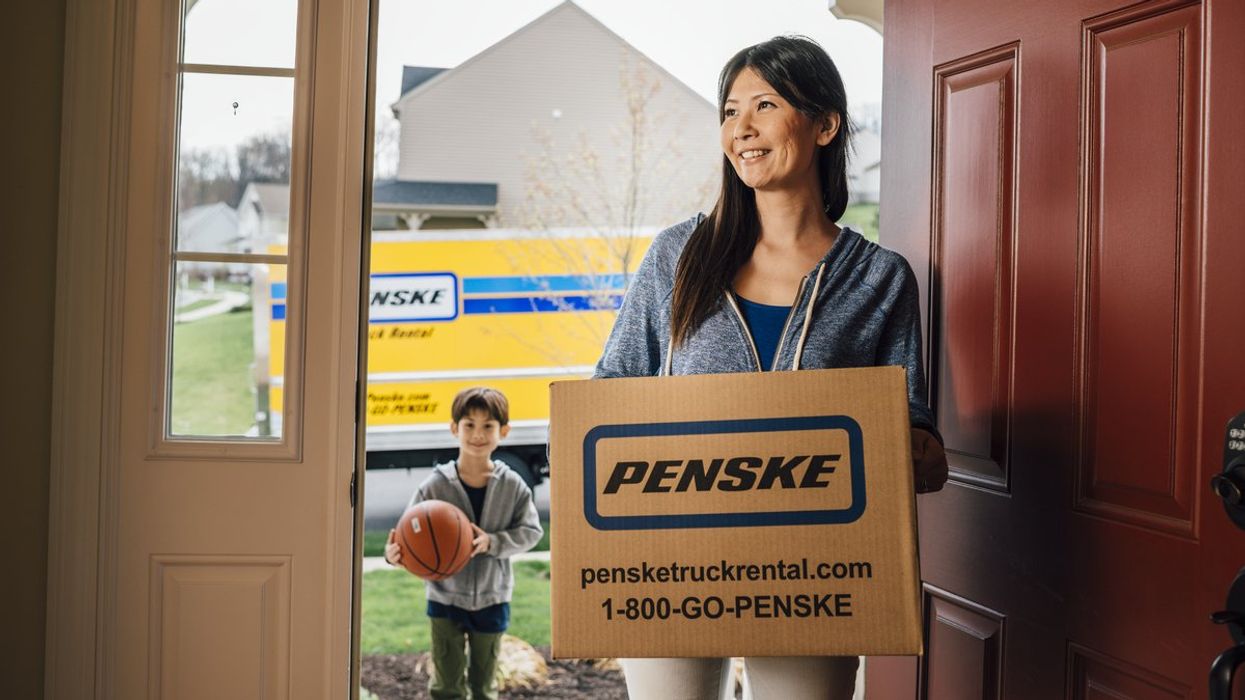 Woman walking through front door carrying a moving box.