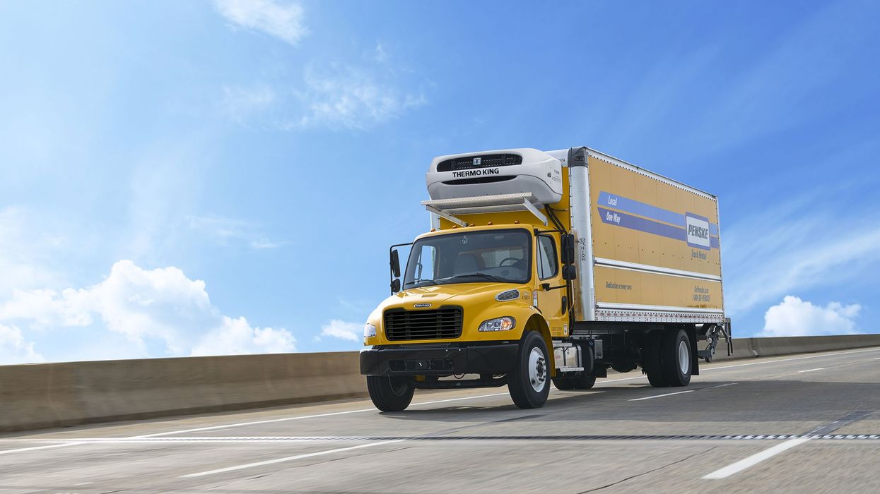 Yellow Penske reefer truck driving over a cement bridge on a sunny day.