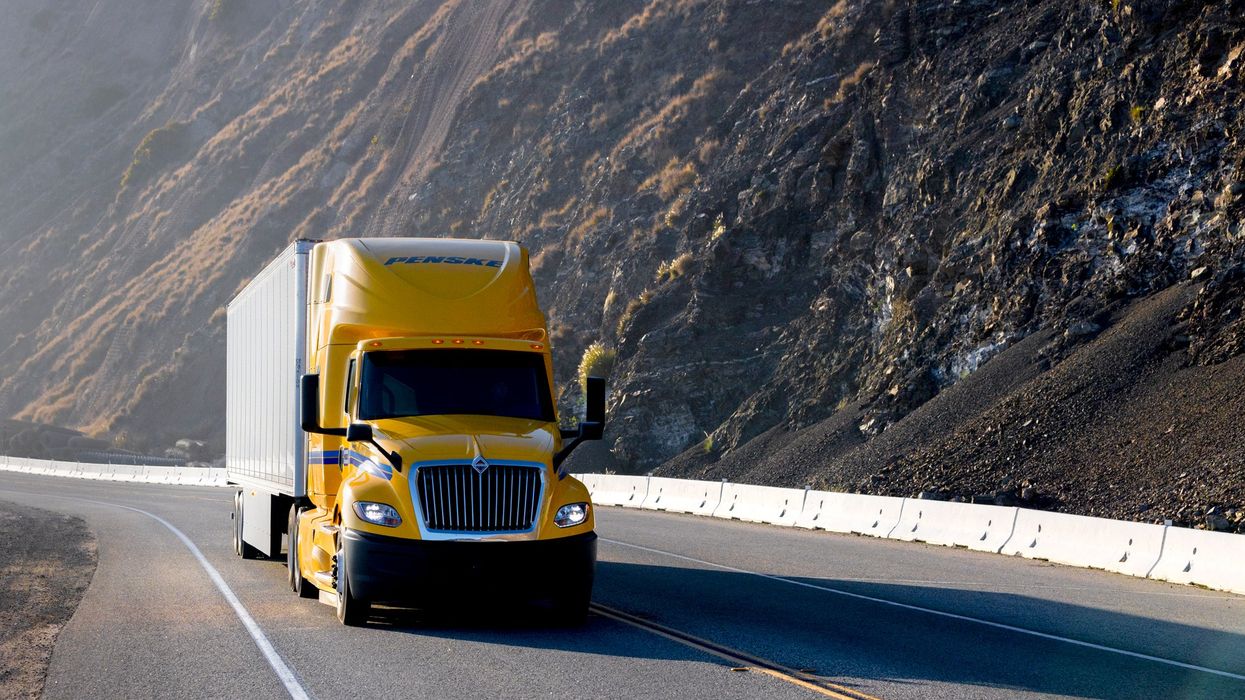 Yellow Penske tractor trailer driving down a highway past mountains