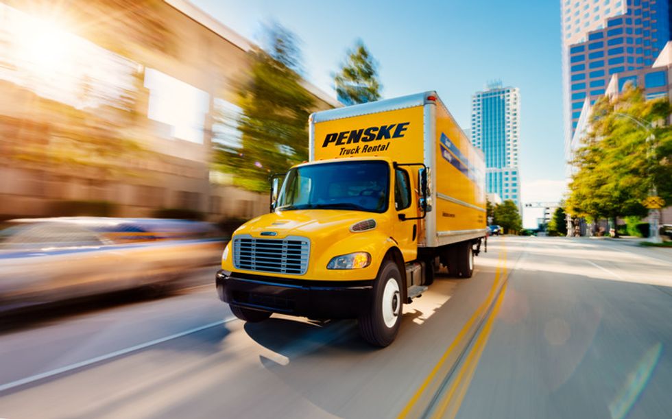 Yellow Penske truck driving through a city